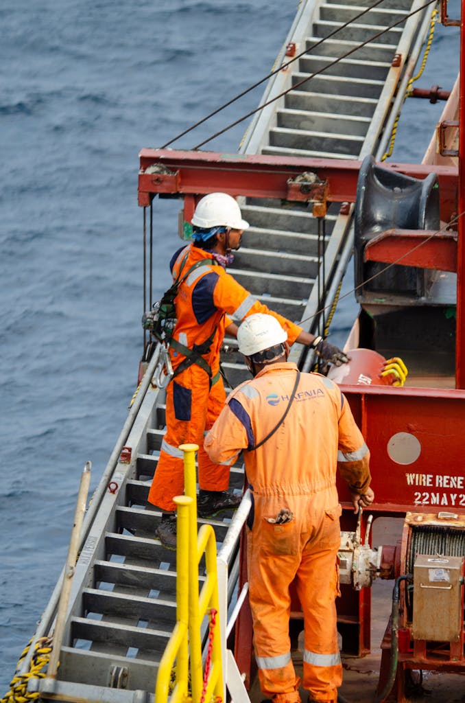 Offshore male workers in orange uniforms maintaining an oil rig at sea.